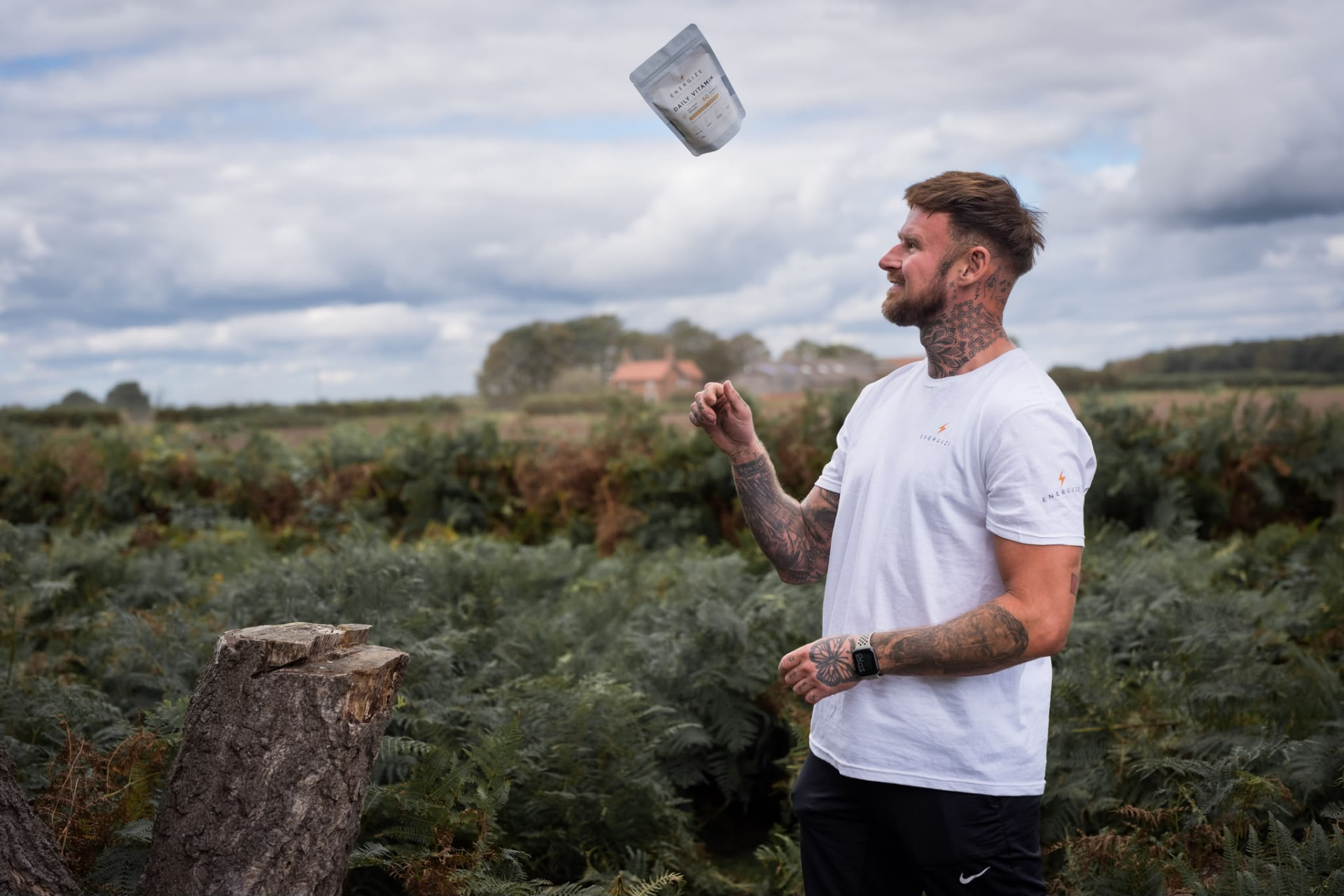 The founder of Energize Luxe outdoors in a fern field, tossing a Daily Vitamin pouch into the air